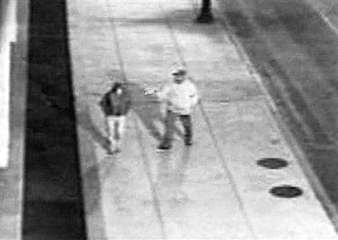 Black and white capture from CCTV footage showing a man pointing a gun at a woman