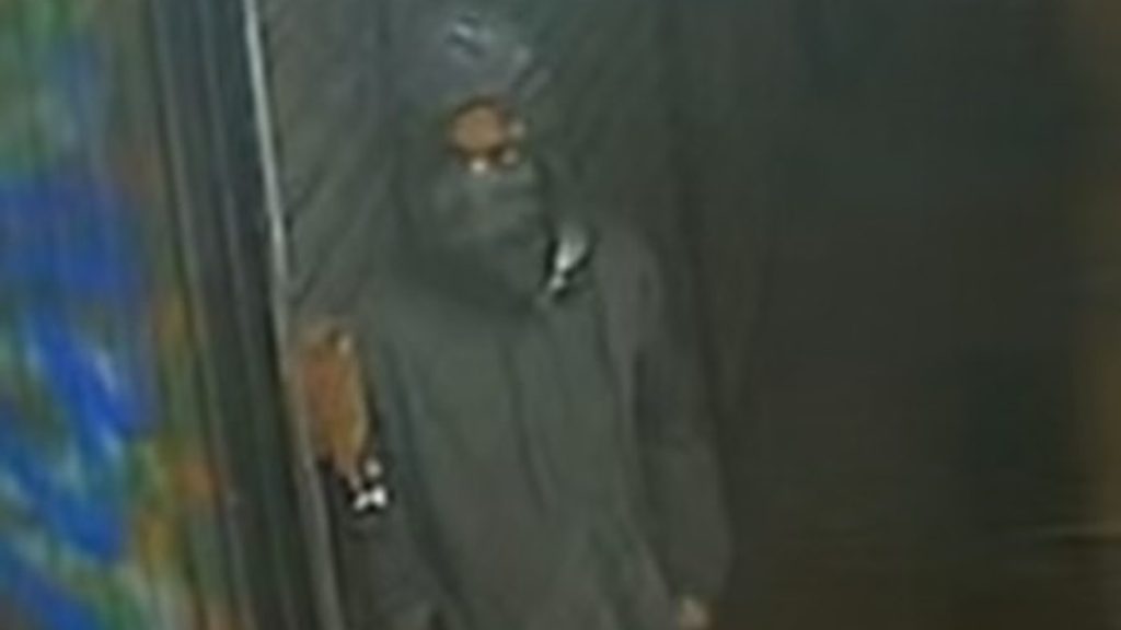 The Queens stabbing suspect leans against a store with his face covered